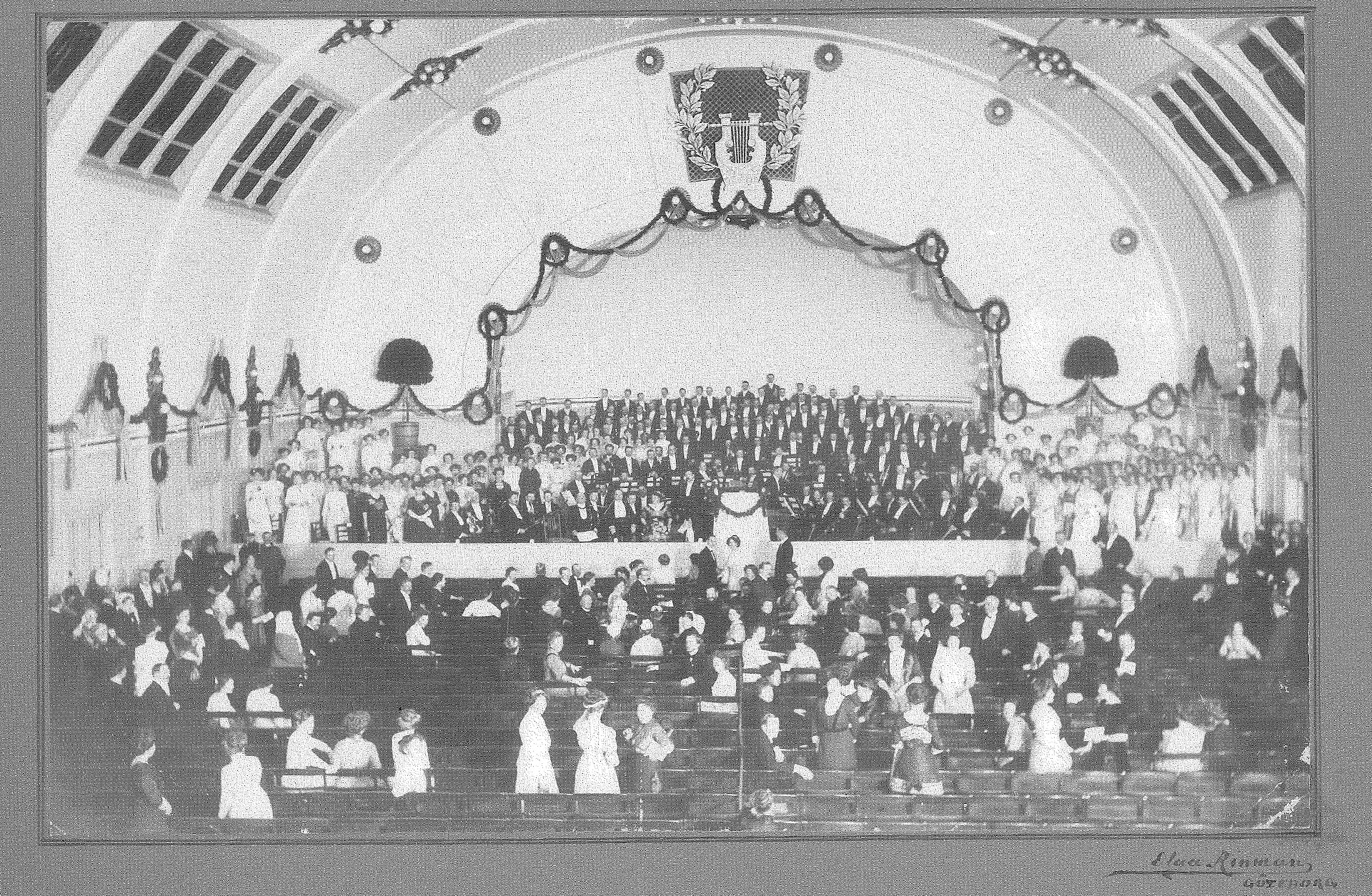 Historiskt fotografi av Göteborgs Symfoniker på scenen i konserthuset på Heden i Göteborg, med publik i förgrunden.