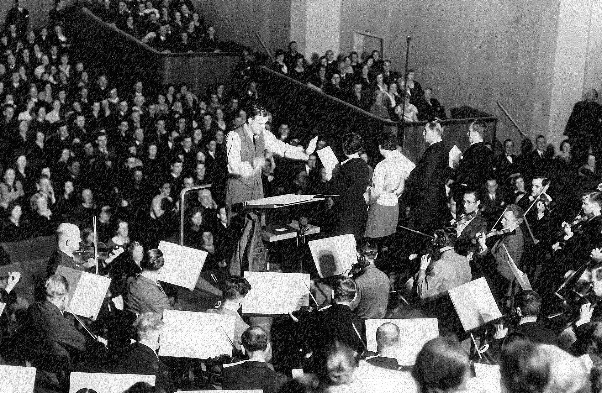Foto av Stora salein i Göteborgs Konserthus vid invigningen 1925, dirigent framför orkester med publiken i salongen i bakgrunden.
