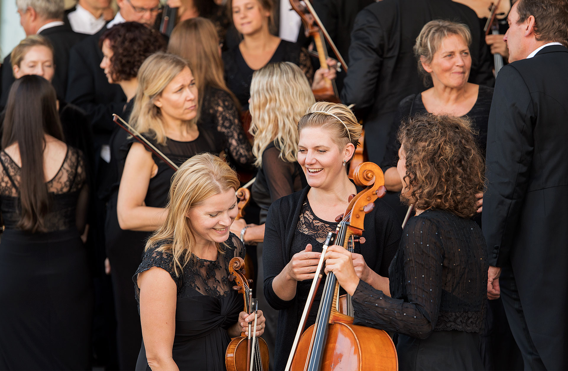 Glada orkestermusiker minglar med sina instrument.