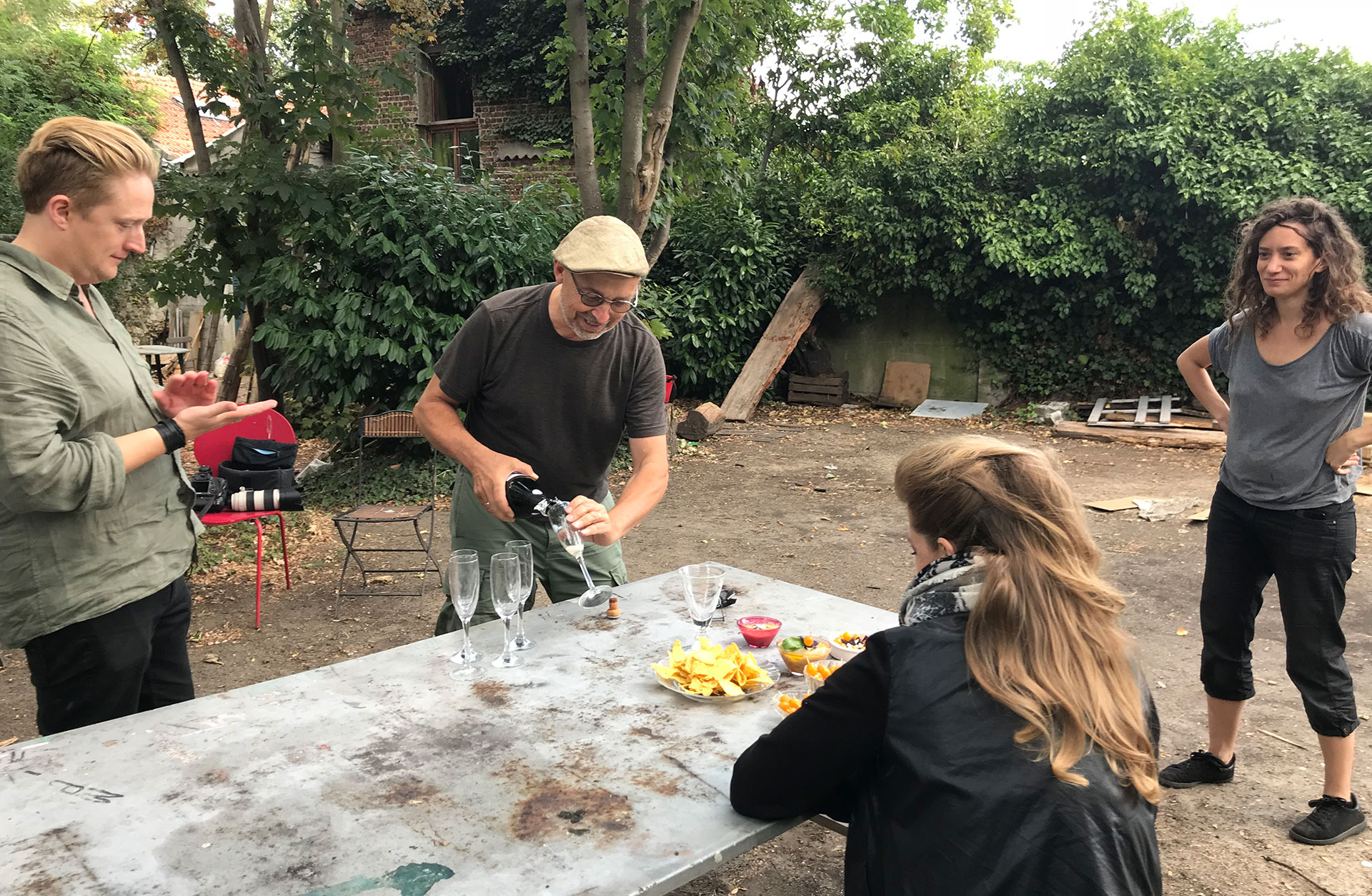 Utomhus i trädgården. Mats häller upp champagne i fem glas. Linus, Julia och Barbara är också där.