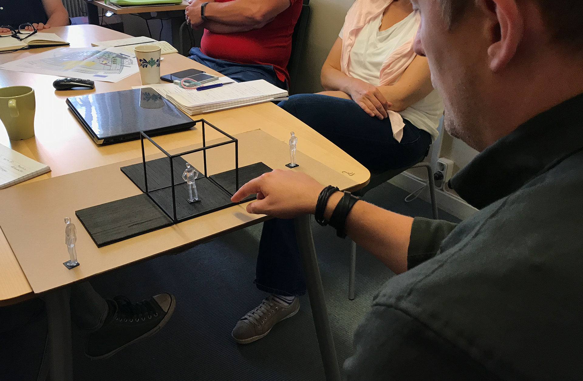 Regissörens Linus Fellbom sitter vid ett bord med människor runt om, och visar upp scenmodellen.