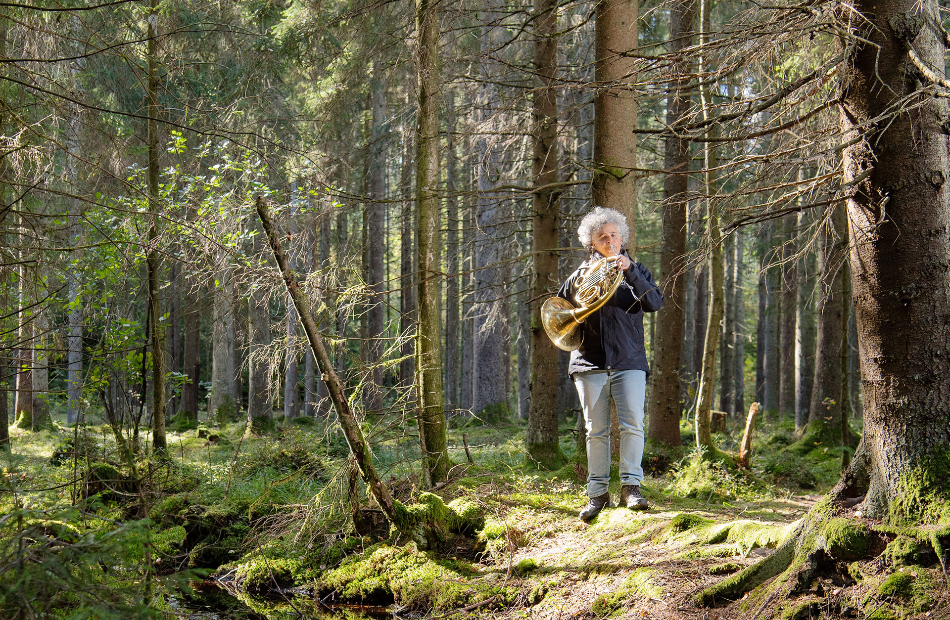 Lisa ford står i skogen och spelar på sitt horn.
