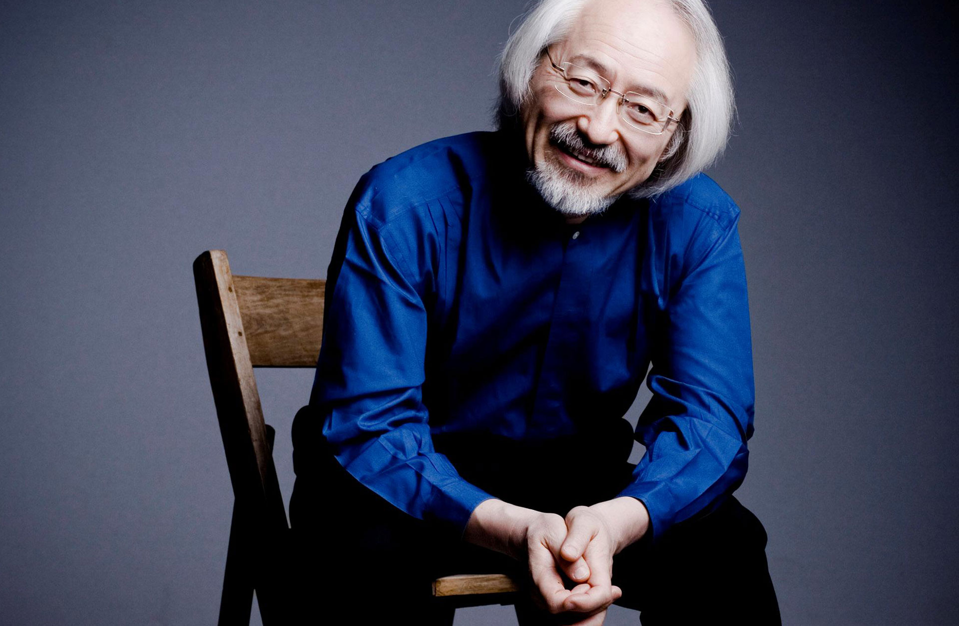 Masaaki Suzuki sitter på en stol. Han ler mot kameran.