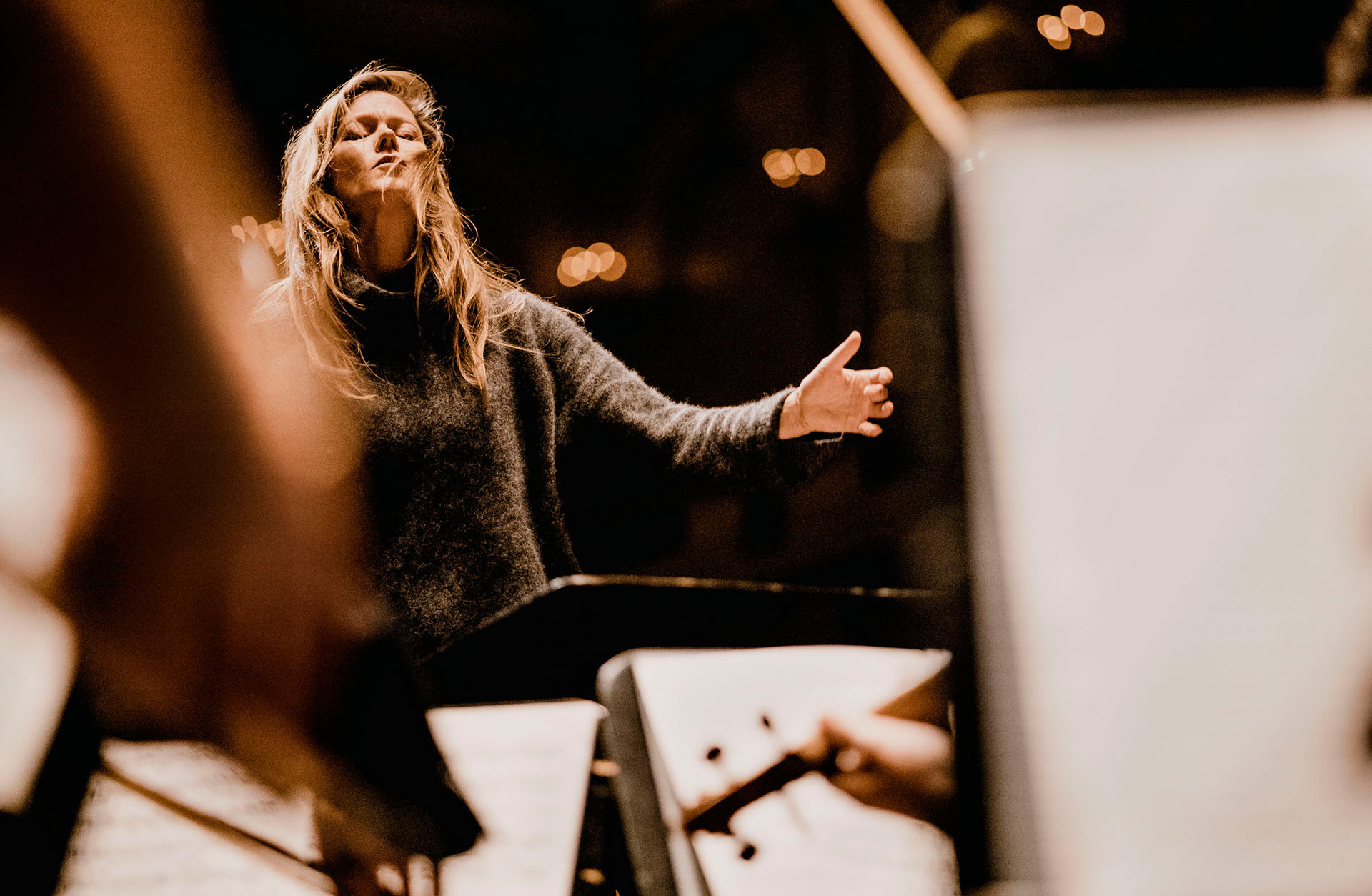 Dirigenten Barbara Hannigan i innerlig pose på pulten, med håret utslaget och händerna framför sig, riktade mot orkestermusikerna.