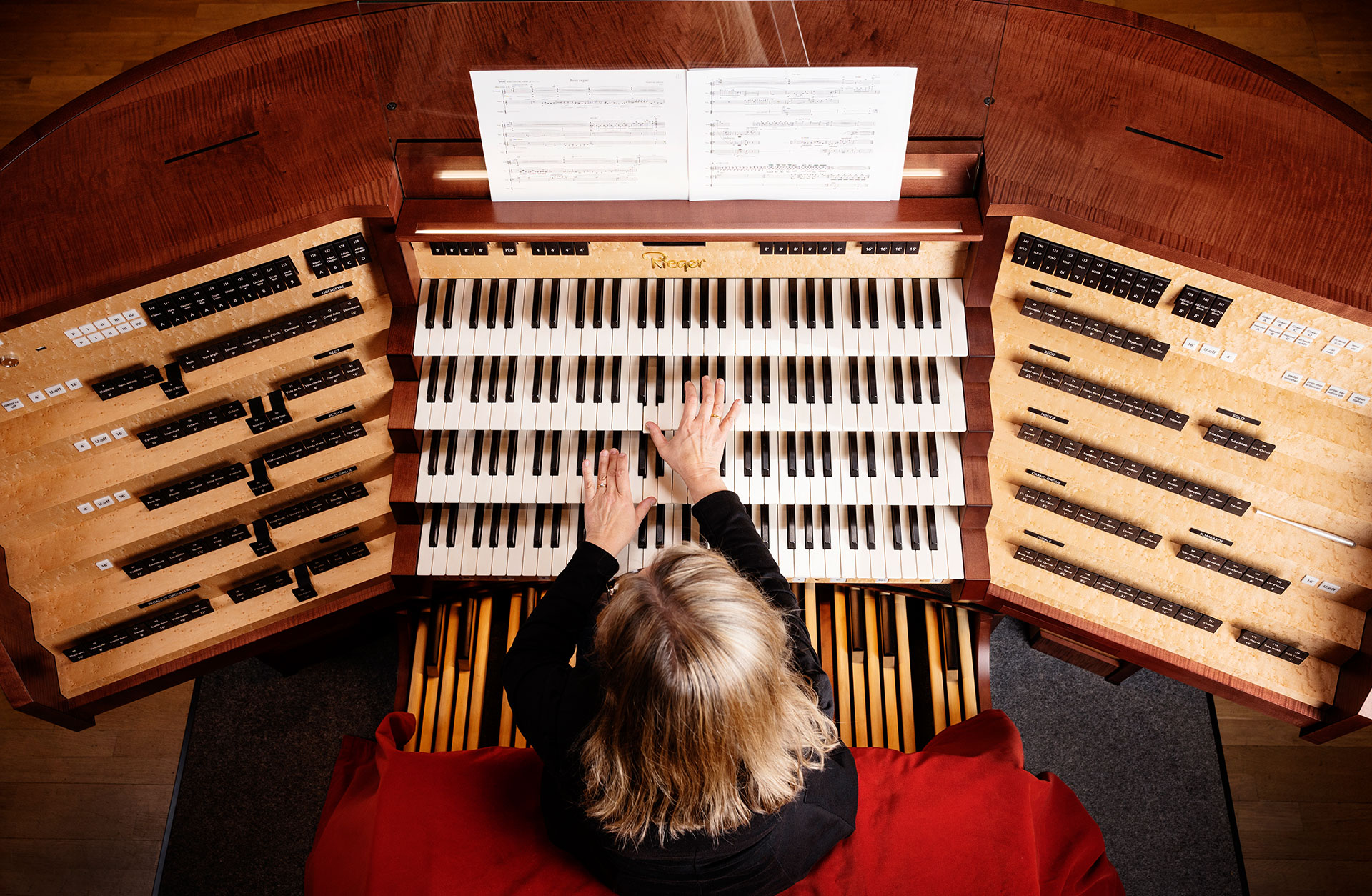 Orgelns spelbord ovanifrån med en mängd tangenter och knappar som musikerns händer vilar på.