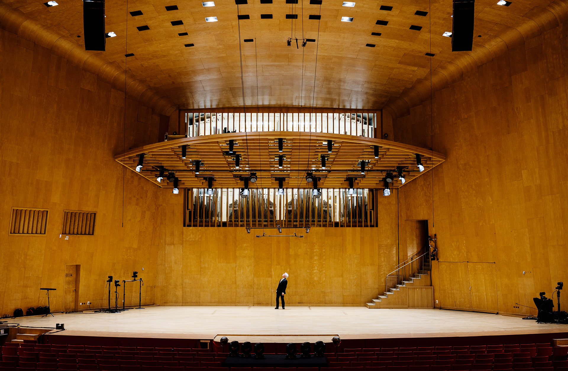 Konserthusorgeln syns mellan lammellerna längst fram i konsertsalen, ovanför scenen. På scenen står en man och blickar upp mot orgeln.