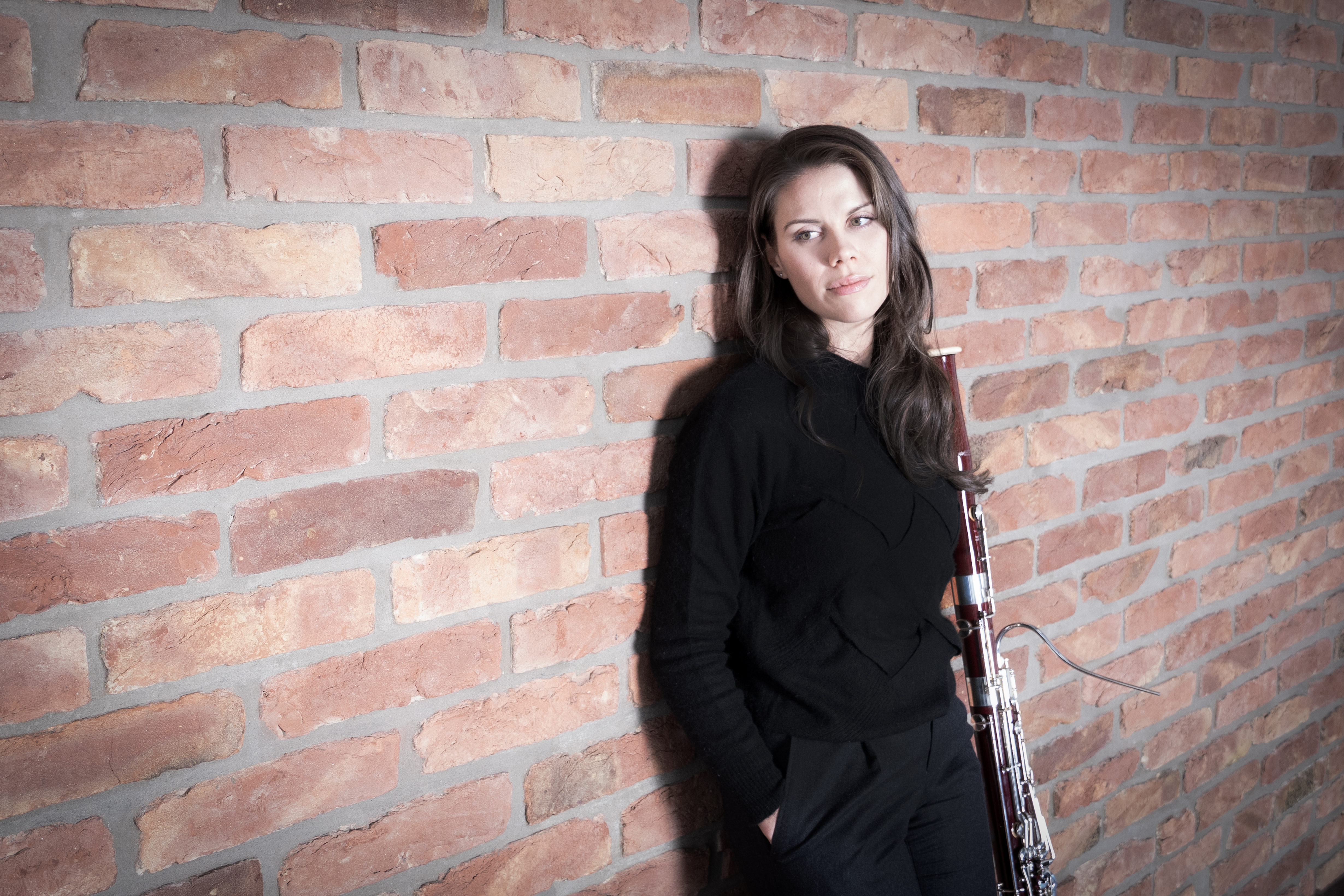 Kaitlyn Cameron, klädd i svarta kläder, lutar sig mot en tegelvägg.