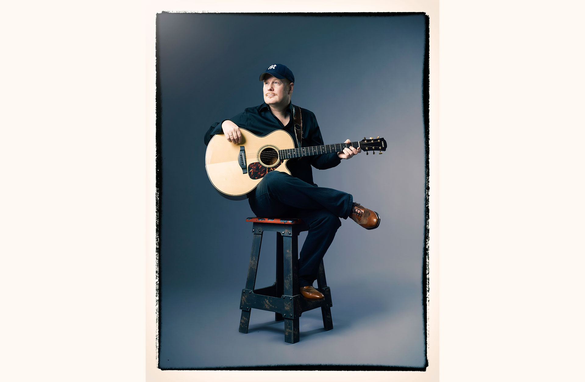 Ulf Wakenius sitter på en barstol med gitarren i famnen.