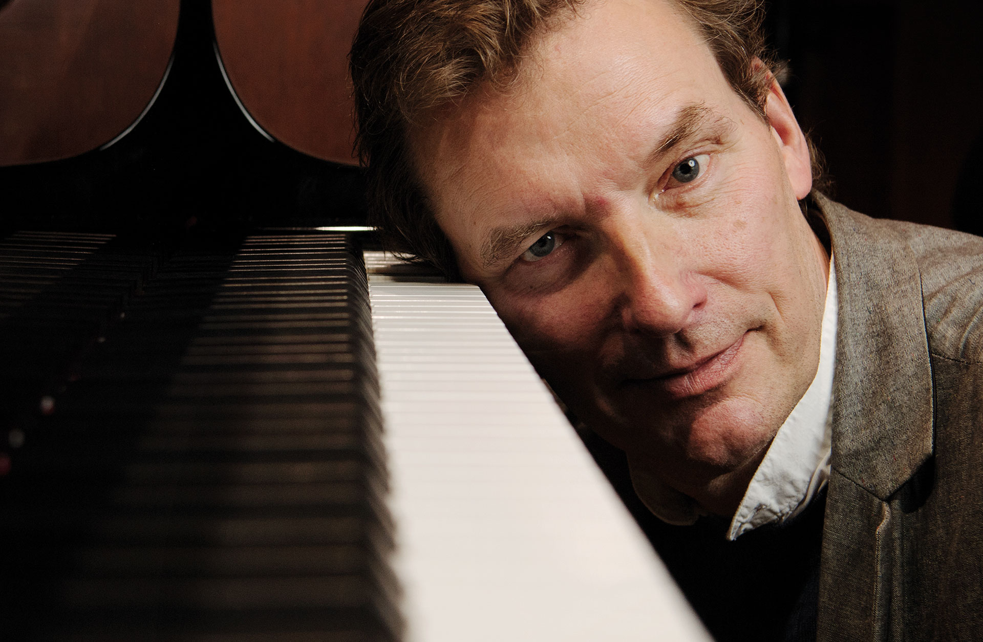 En sittande man lutar sitt huvud mot ett piano