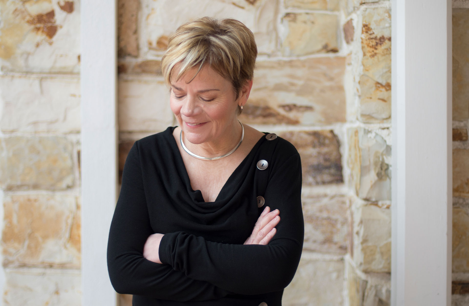 Porträtt av Marin Alsop, i halvfigur, mot en stenvägg.