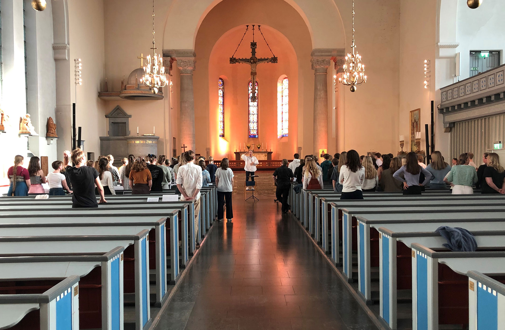 Ungdomskör repeterar i krykan med dirigenten framför sig.