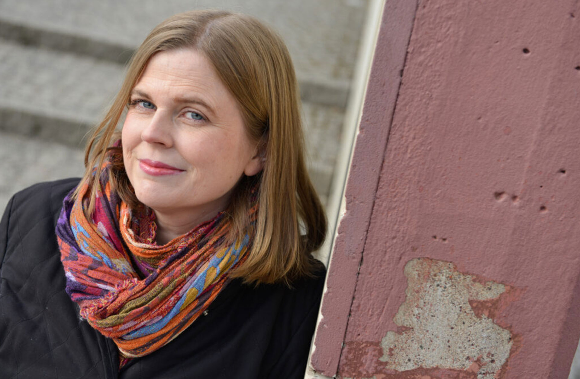 Brita Byström utomhus, står lutad mot en vägg av betong.