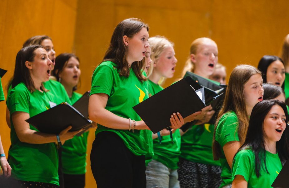 Flera ungdomar står med pärmar i händerna och sjunger tillsammans i kör.