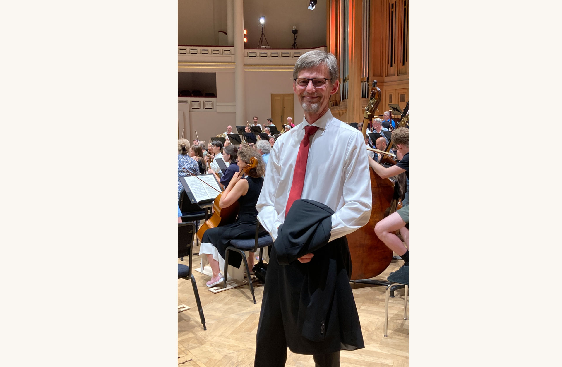 Johan Nordin står vid sidan av orkestern. Han är finklädd och ler .