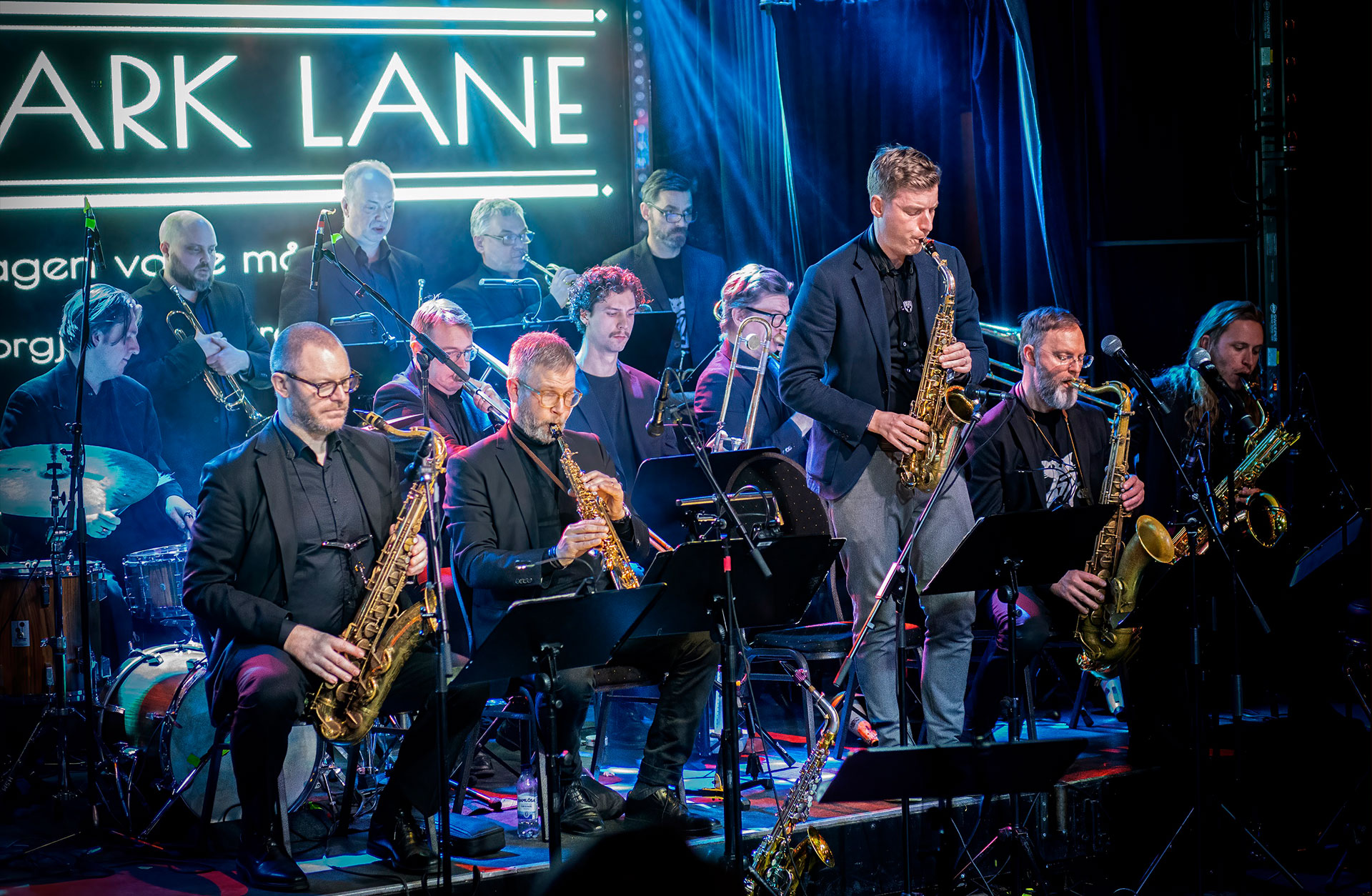 Ett storband med saxofoner, tromboner, trumpeter och kompgrupp på scenen.