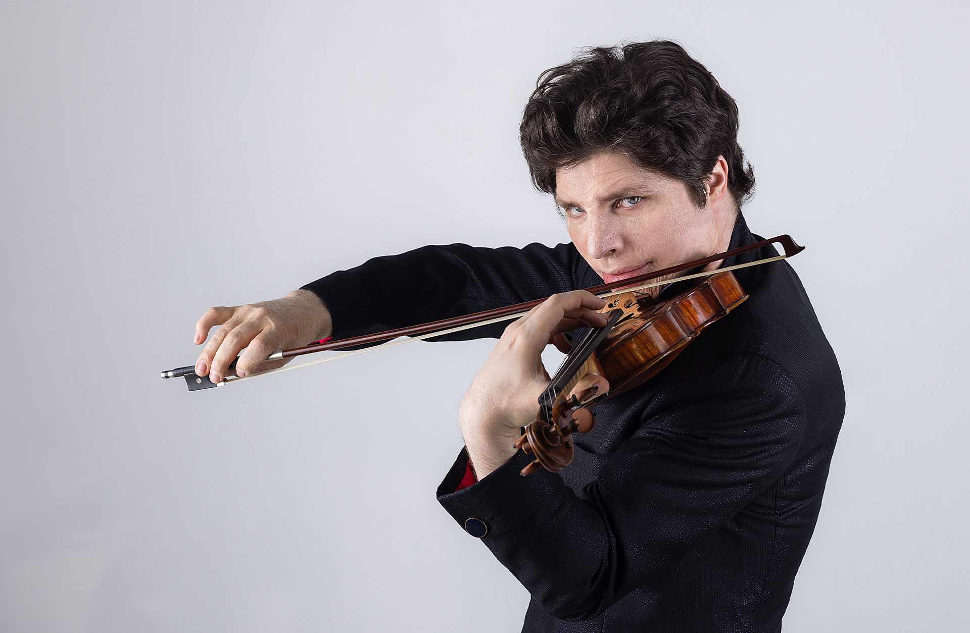 Man tittar in i kameran och spelar violin. Svartklädd mot vit bakgrund.