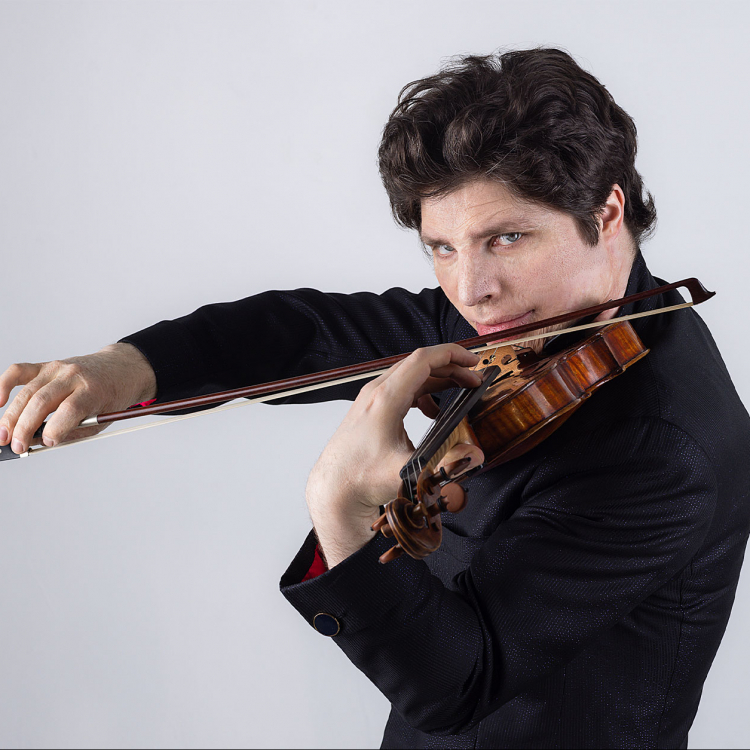 Man tittar in i kameran och spelar violin. Svartklädd mot vit bakgrund.