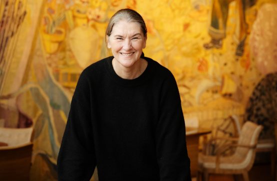 En glad Anna-Karin Larsson står vid gobelängen i Götaplatsfoajen. Hon ler stort.