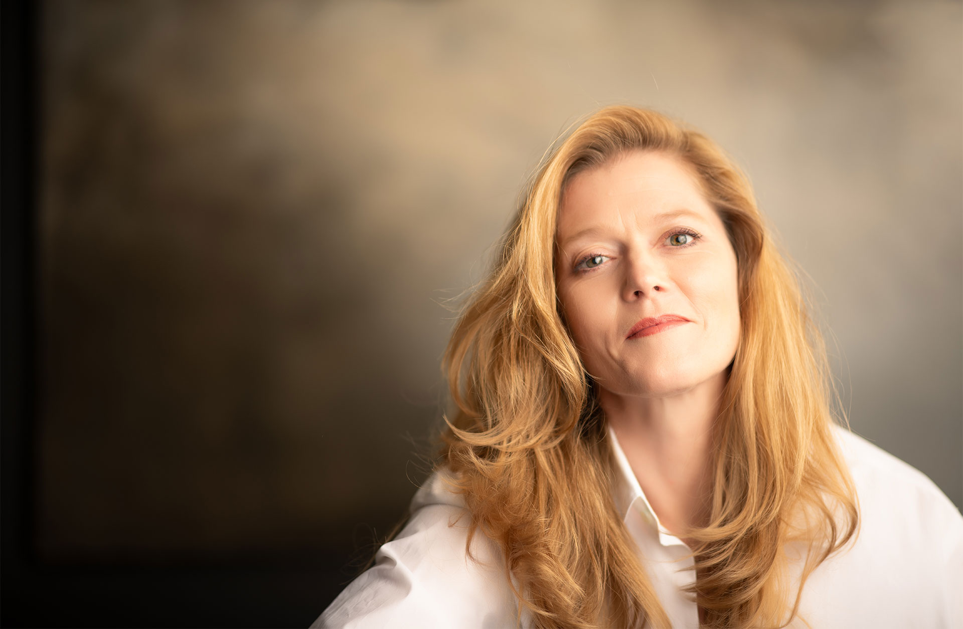 Halvkroppsporträtt av Barbara Hannigan. Hon ler och tittar in i kameran. Hon ar vit skjorta och hennes långa hår faller över axlarna.