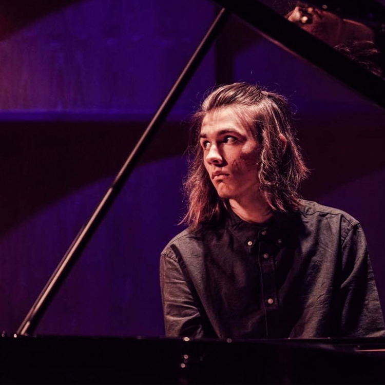 En ung man med axellångt hår spelar piano.