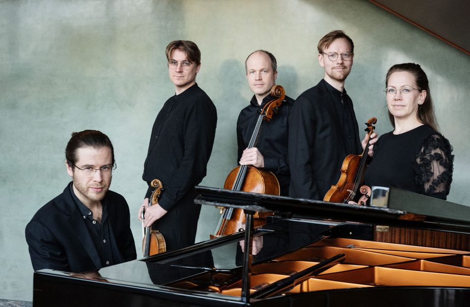 En kammarkvartett står vid en flygel. Vid flygeln sitter pianisten Magnus Fryklund, bakom står fyra stråkmusiker.