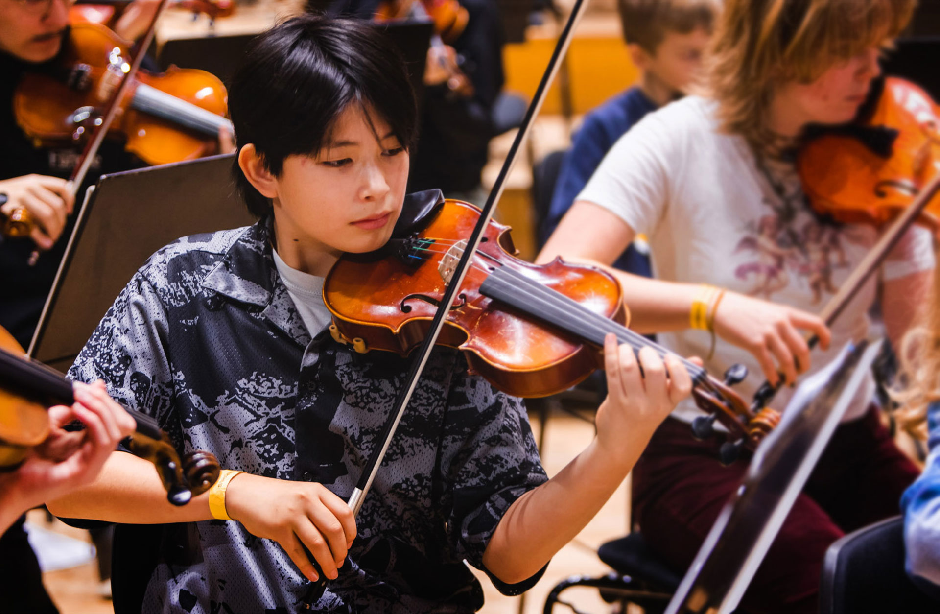 En ung man med svart kortklippt hår sitter i orkestern och spelar viola.