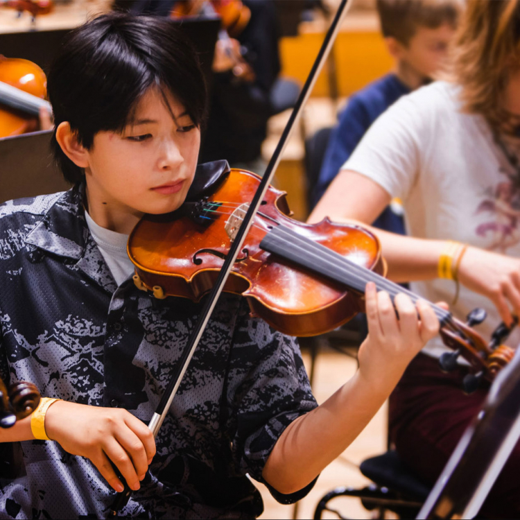 En ung man med svart kortklippt hår sitter i orkestern och spelar viola.