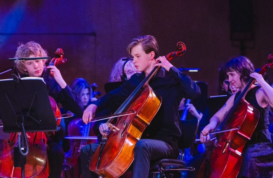 Ungdomar ur cellosektionen spellar koncentrerat under en konsert.