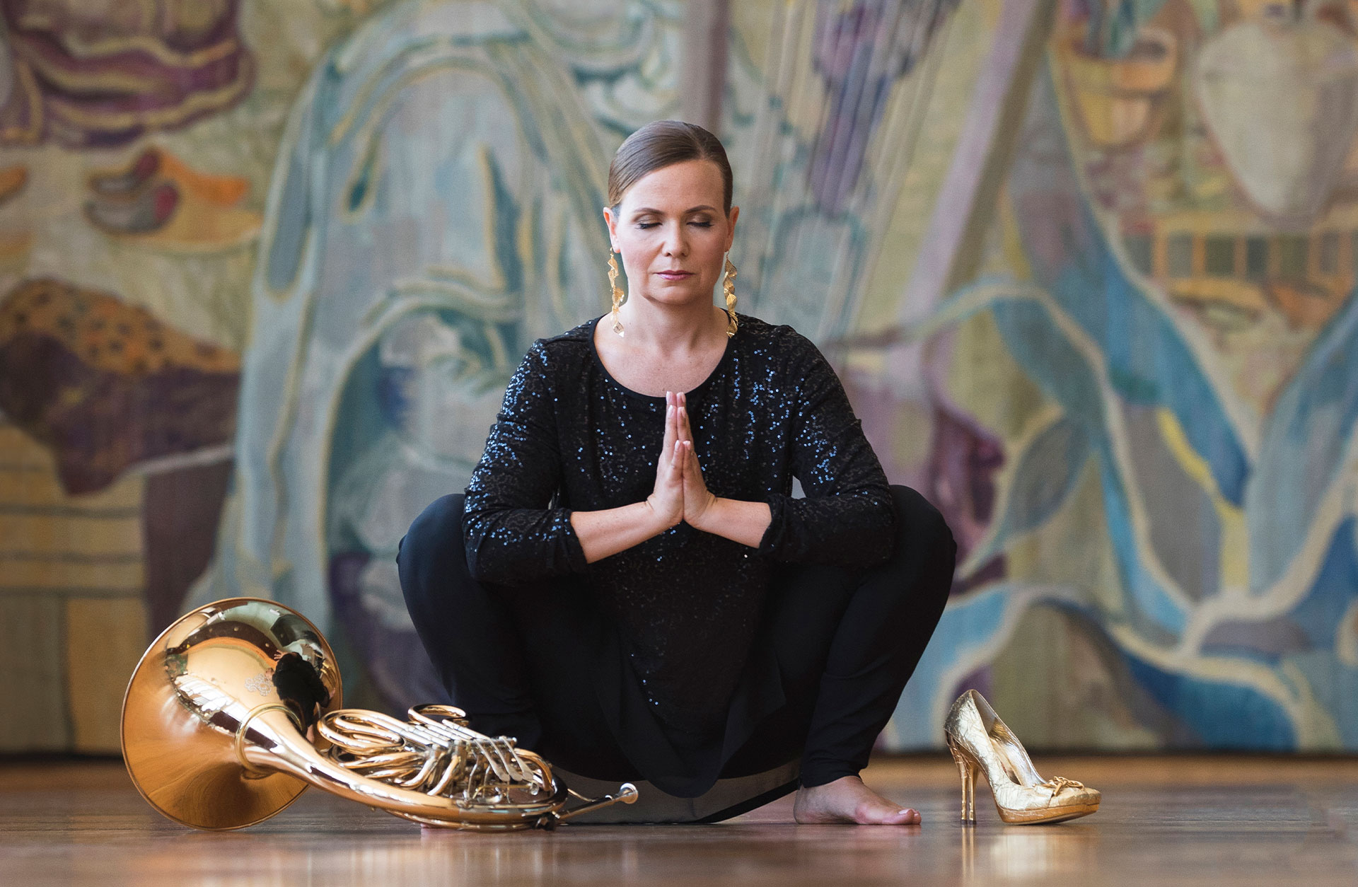 En finklädd sminkad kvinna sitter i en hukad yogaposition och blundar. Det ligger ett horn bredvid henne.