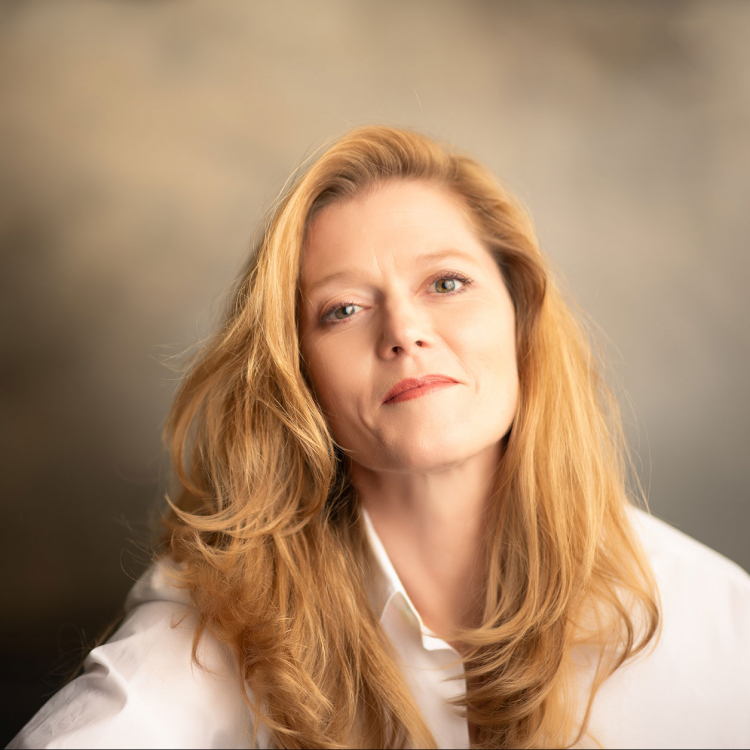 Halvkroppsporträtt av Barbara Hannigan. Hon ler och tittar in i kameran. Hon ar vit skjorta och hennes långa hår faller över axlarna.