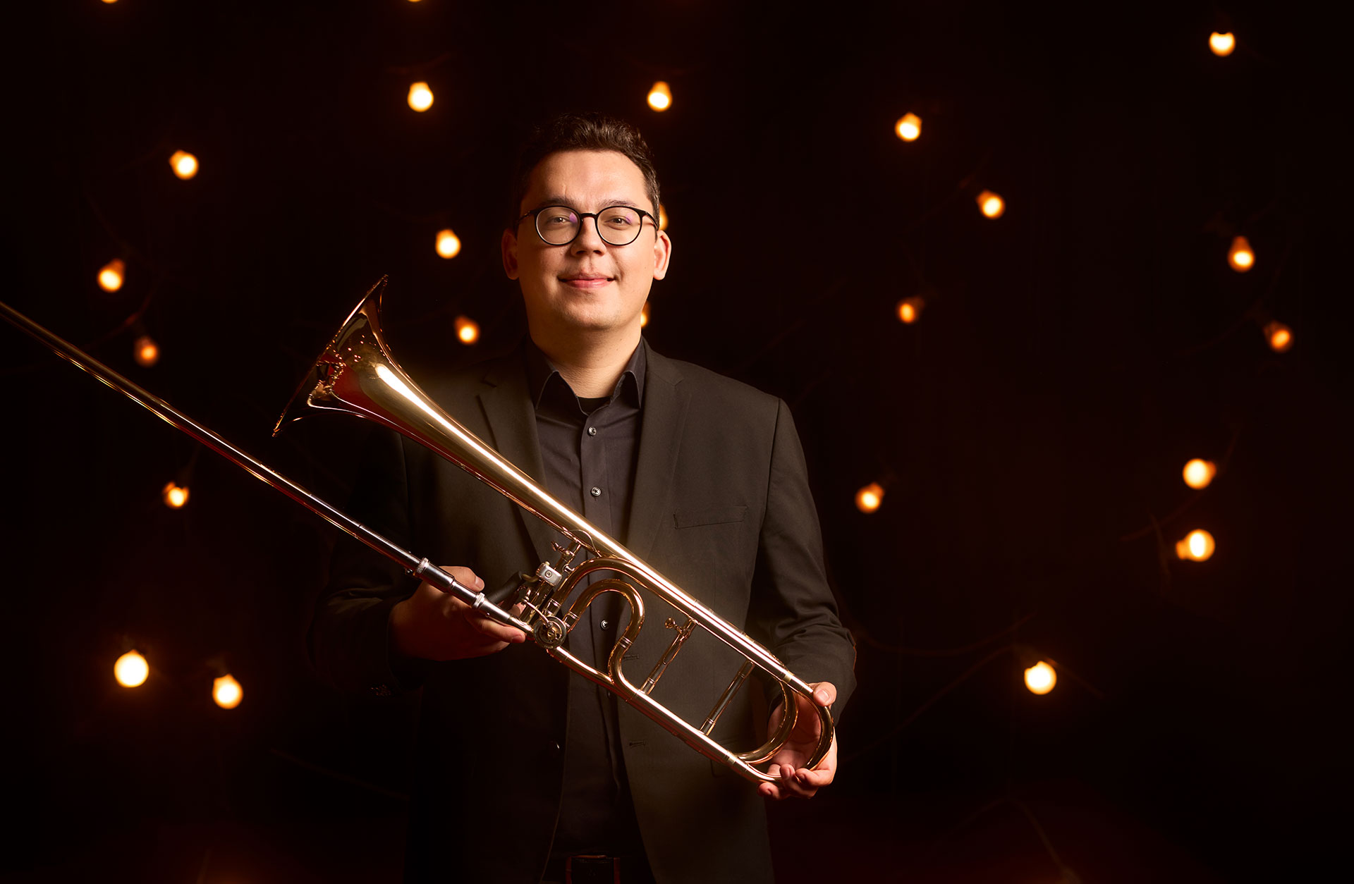 Musiker står med sin trombon mot en bakgrund av glödlampor