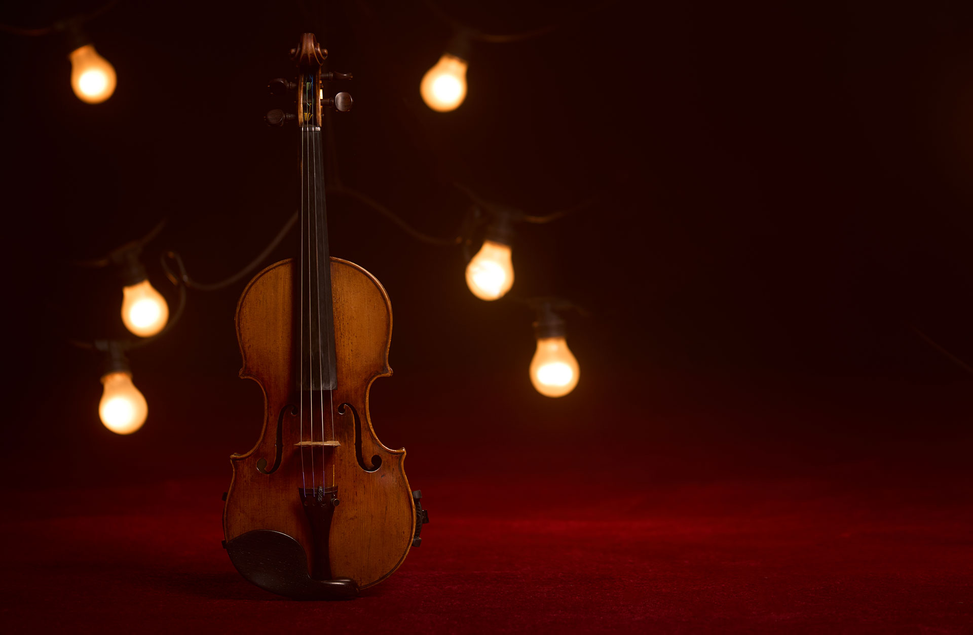 En violin på en röd matta med stämningsfullt ljus.