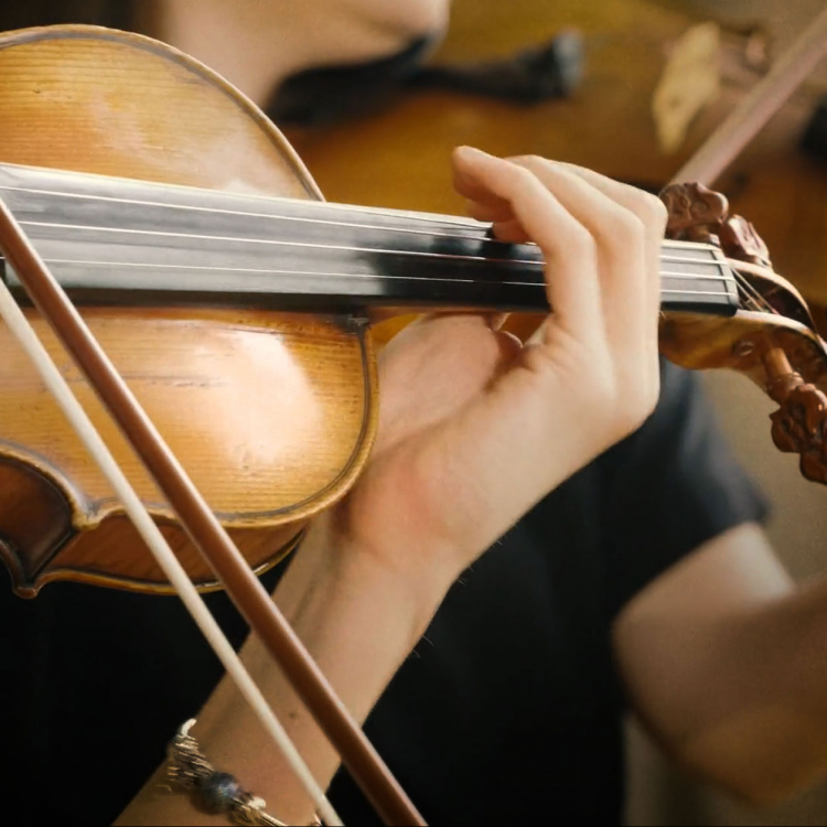 Närbild av en violin och en hand som spelar på strängarna.
