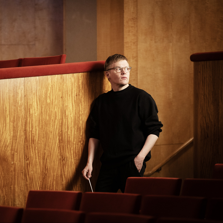 Pekka Kuusisto står lutad mot en vägg i trä