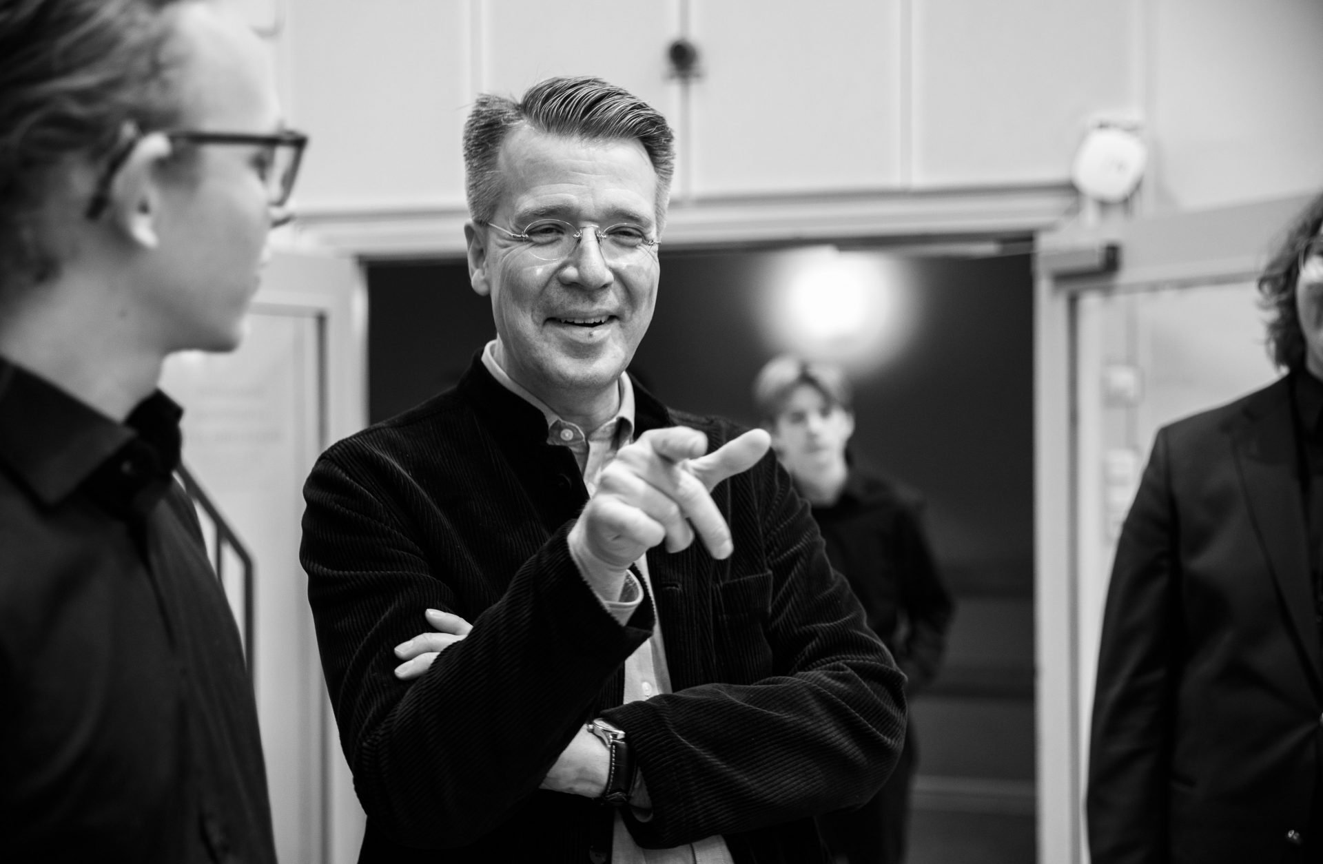 Dirigent Andreas Hansson pekar med handen mot kameran och ler. Svartvit bild. 