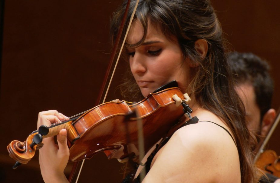 Violinist Ava Bahari står med sitt instrument och spelar under en konsert med mörk omgivning.