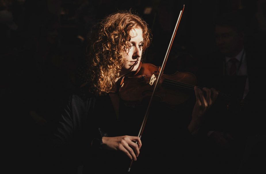 Violinist Clara Garde står i mörk omgivning och spelar violin