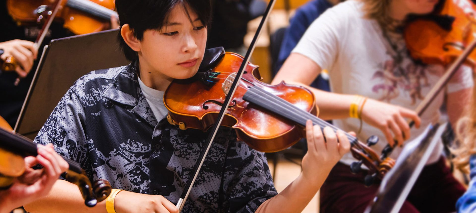 Ung violinist spelar på sitt instrument på scen, omgiven av andra unga musiker.