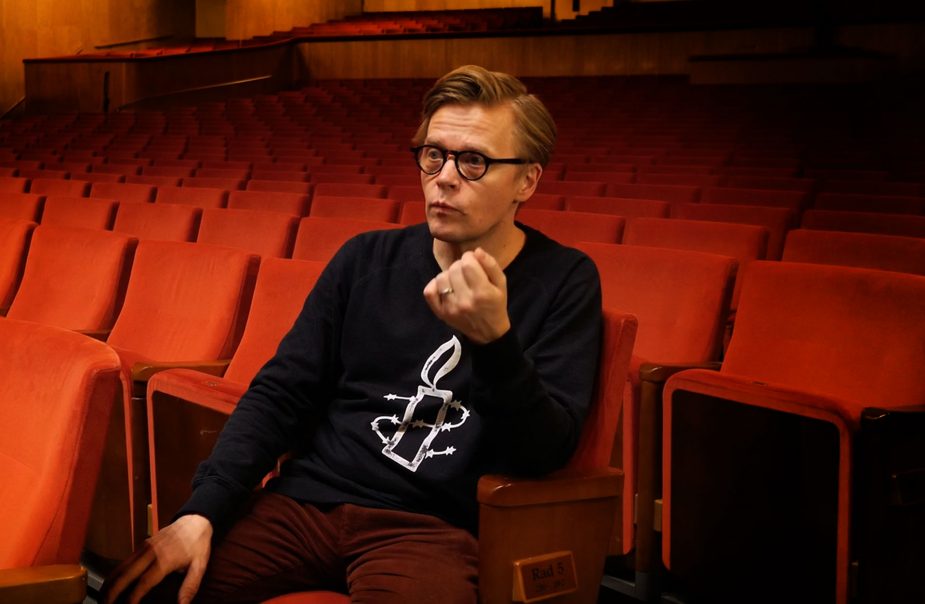 Dirigent Pekka Kuusisto sitter i Stora salens röda stolar och pratar.