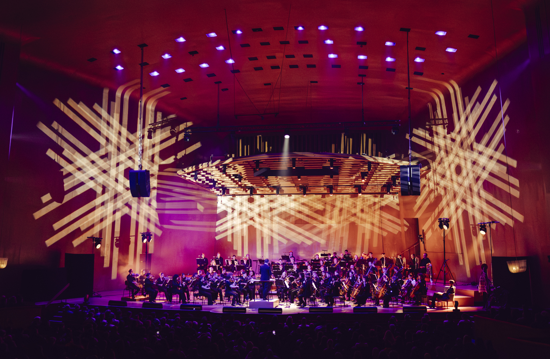 Ungdomar i en symfoniorkester på scenen med stämningsfull ljussättning.